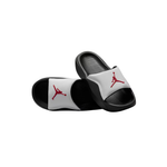 A pair of black and white slide sandals featuring the red Jumpman logo on the straps, displayed against a solid white background.