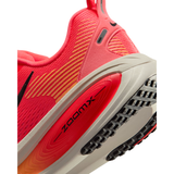 Close-up of a Nike running shoe showing the midfoot and heel area, featuring a bright coral pink mesh upper with diagonal yellow stripes, a red ZoomX cushioning unit, and a beige and black outsole.
