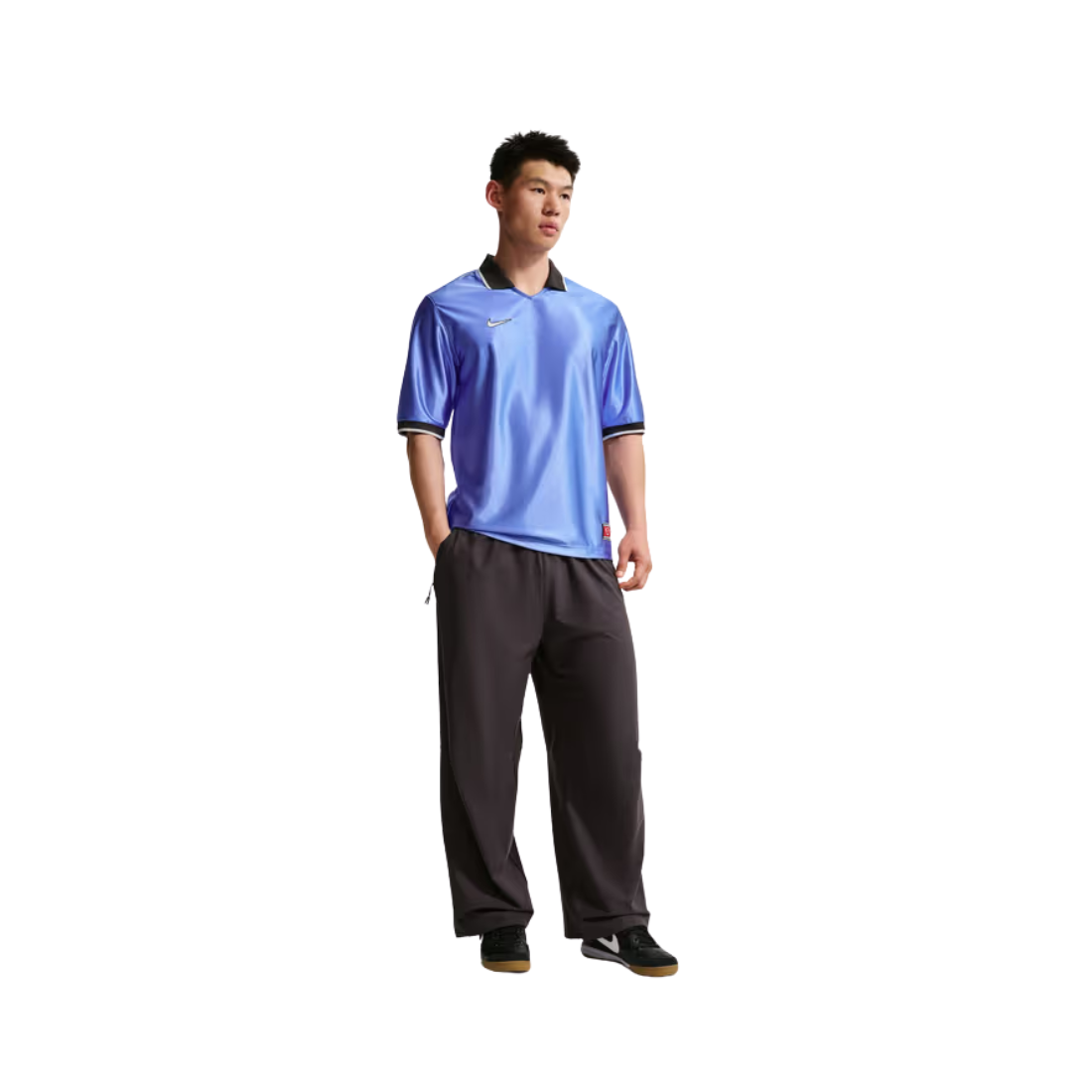 A man modeling a short-sleeve athletic polo shirt in a vibrant blue color with black and white trim, paired with dark gray sweatpants and black sneakers, set against a plain white background.