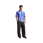 A man modeling a short-sleeve athletic polo shirt in a vibrant blue color with black and white trim, paired with dark gray sweatpants and black sneakers, set against a plain white background.