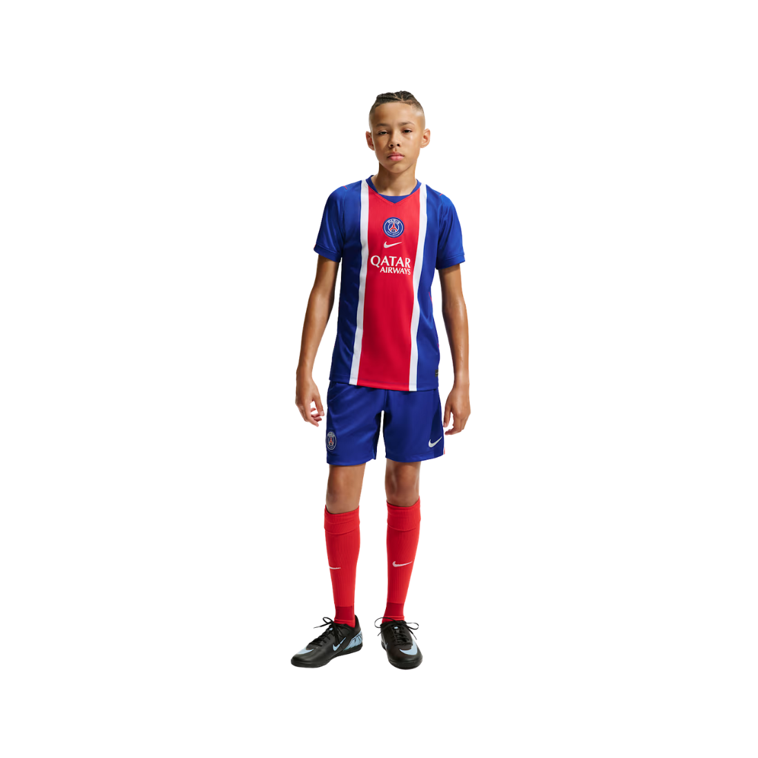 A young boy modeling a Paris Saint-Germain soccer kit, featuring a blue, red, and white jersey with 'QATAR AIRWAYS' sponsor logo, matching blue shorts, red socks, and black soccer shoes, set against a plain white background.