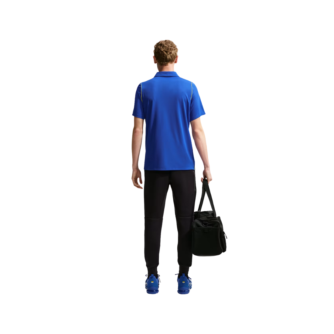 A man shown from behind wearing a bright blue short-sleeve polo shirt, black athletic pants, and blue sneakers, while carrying a black duffel bag against a plain white background.
