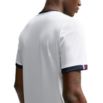 A close-up back view of a person wearing a white short-sleeve athletic jersey with dark navy trim at the collar and sleeve cuffs, plus a small red and white stripe on one cuff.