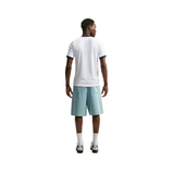 A man viewed from behind wearing a white short-sleeve t-shirt with navy blue trim, light blue denim shorts, white socks, and sneakers, set against a plain white background.