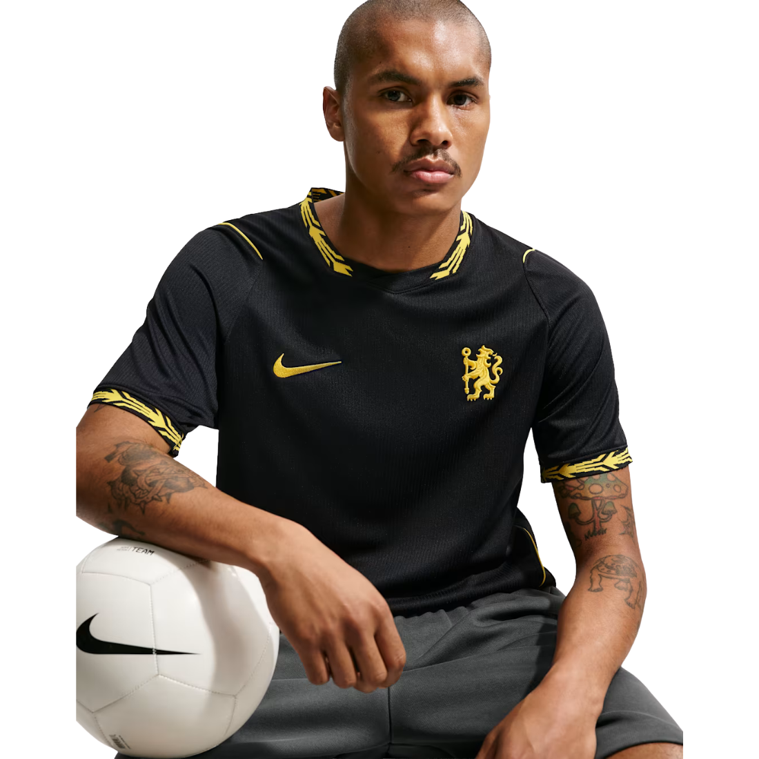 A man wearing a black Nike Chelsea soccer jersey with gold trim and crest, holding a white soccer ball against a white studio background.