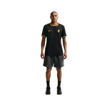 A male model stands against a solid white background wearing a black Nike soccer jersey with yellow accents and dark gray shorts.