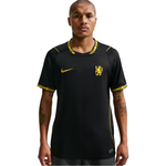 A man modeling a black Chelsea FC Nike soccer jersey with yellow accents, including the Nike swoosh and club crest, against a plain white background.