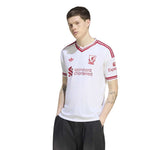 A man modeling a white Adidas Liverpool football jersey with red stripes and sponsor logos, paired with black trousers, against a plain white background.