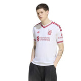 A man modeling a white Adidas Liverpool football jersey with red stripes and sponsor logos, paired with black trousers, against a plain white background.