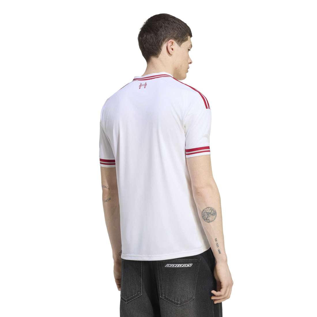 A man shown from the back wearing a white Under Armour short-sleeve athletic jersey with red stripes on the shoulders and sleeves, paired with dark gray jeans.