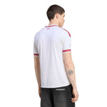 A man shown from the back wearing a white Under Armour short-sleeve athletic jersey with red stripes on the shoulders and sleeves, paired with dark gray jeans.