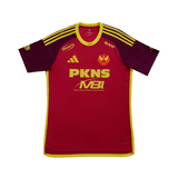 A red and maroon short-sleeve sports jersey with yellow trim, featuring the PKNS MBI logo on the front, an Adidas logo, and a team crest, displayed on a solid white background.