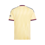 A pale yellow short-sleeve soccer jersey shown from the back, featuring navy and red striped trim on the collar and sleeve cuffs, with a partial black 'el.' logo on the right sleeve.